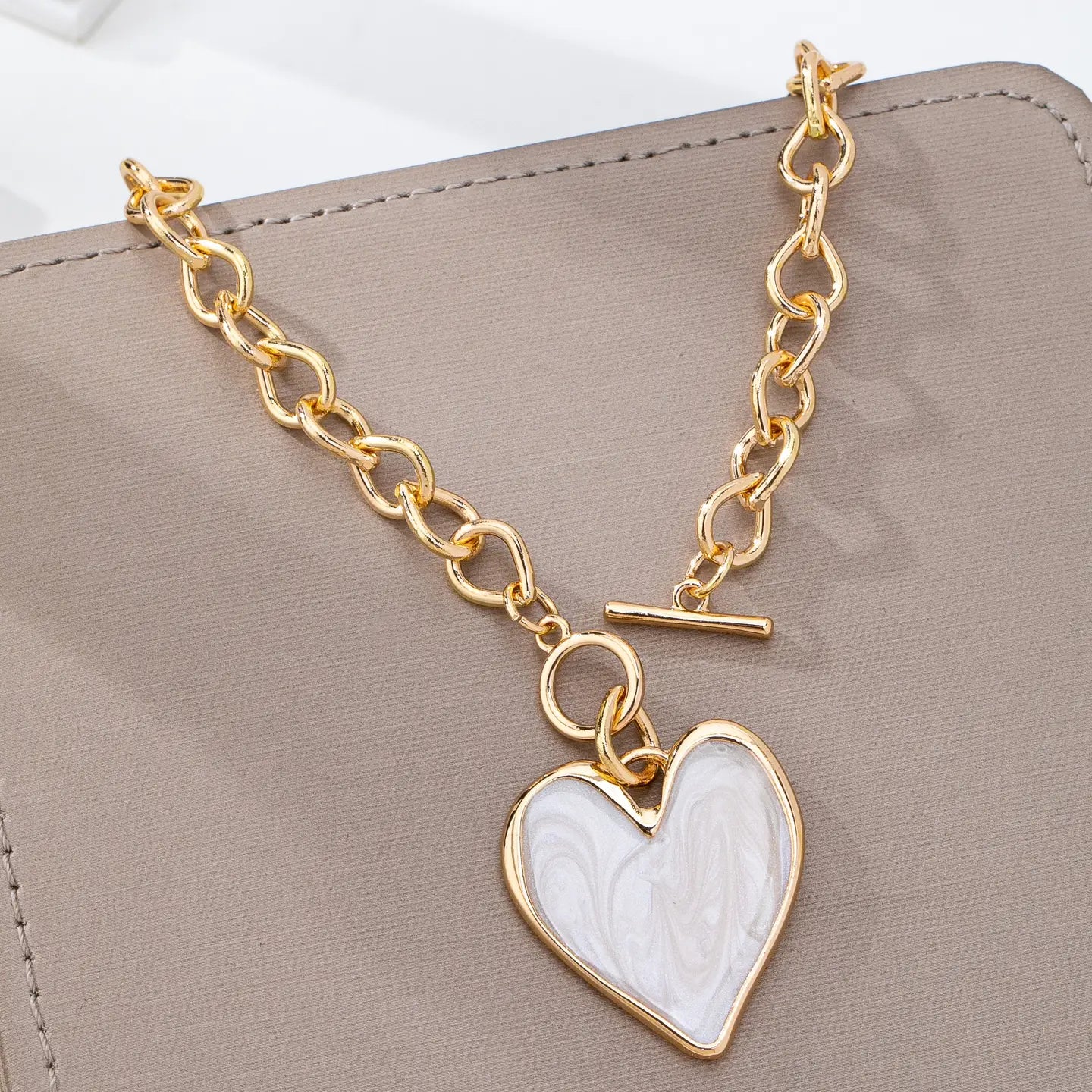 Gold bracelet with a heart-shaped white pendant on a beige surface
