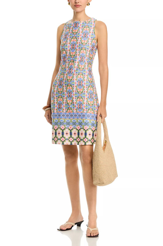 Woman wearing a patterned dress holding a straw bag on a white background