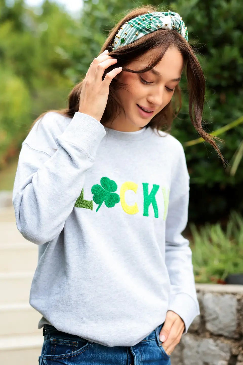 Person wearing a gray sweatshirt with 'LUCKY' and a clover design outdoors.