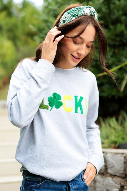 Person wearing a gray sweatshirt with 'LUCKY' and a clover design outdoors.