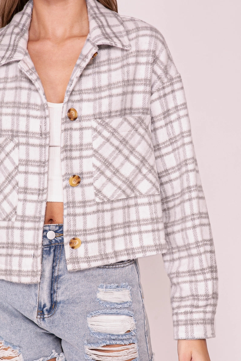 A cropped long-sleeve plaid button-front jacket in a light gray and white check pattern, styled open over a white top and paired with distressed light-wash blue jeans.