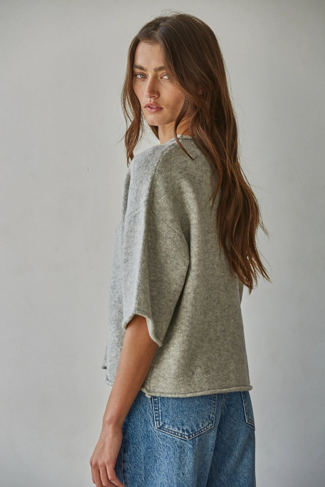 Woman wearing a gray sweater and blue jeans against a plain background