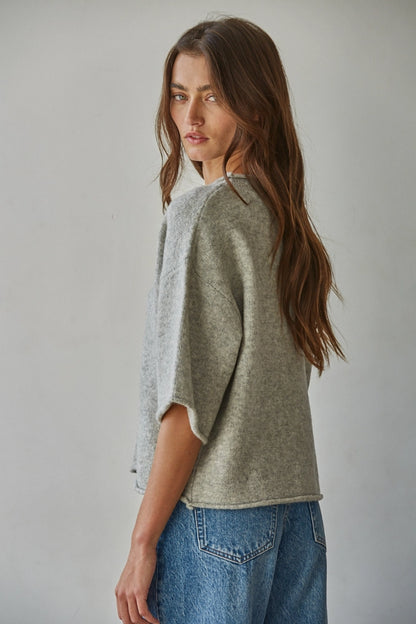 Woman wearing a gray sweater and blue jeans against a plain background