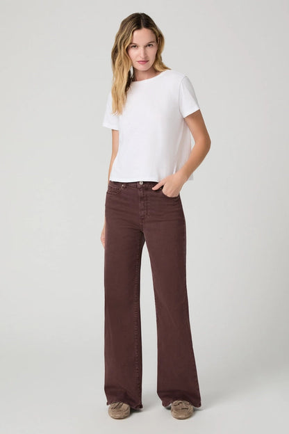 A woman modeling a white short-sleeve crewneck t-shirt and dark brown wide-leg jeans against a light gray studio background.
