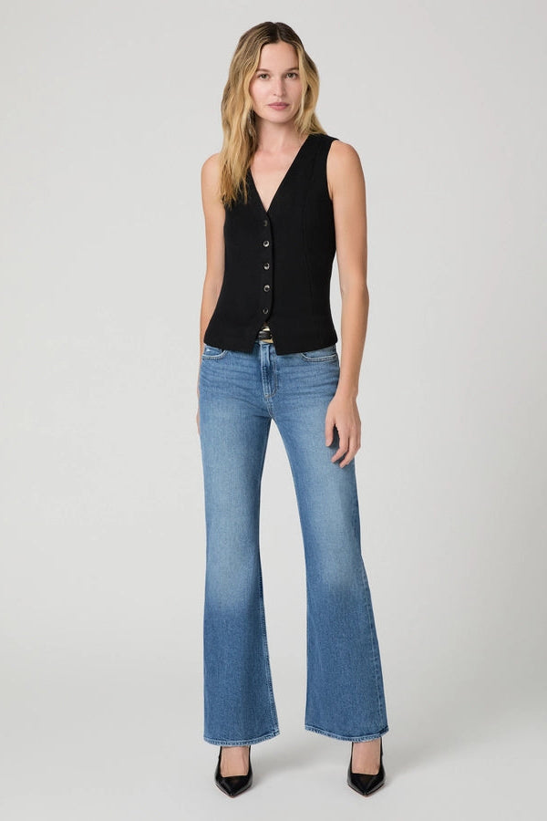 A woman modeling a sleeveless black button-front vest and blue flare jeans against a light gray studio background.