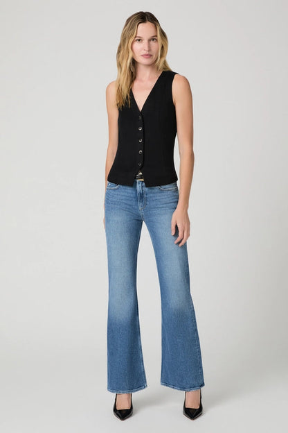 A woman modeling a sleeveless black button-front vest and blue flare jeans against a light gray studio background.