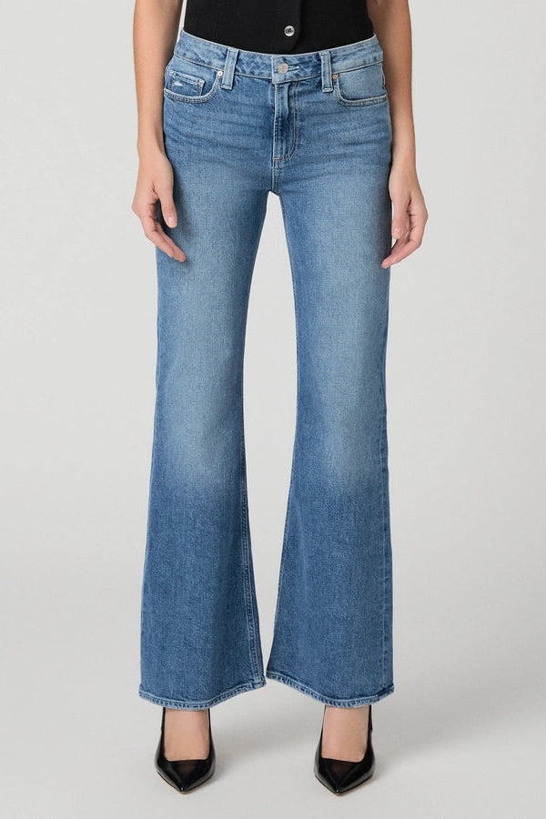 A model wearing a pair of medium-wash blue flare jeans with a faded wash effect, paired with a black top and black pointed-toe heels, photographed against a light gray studio background.