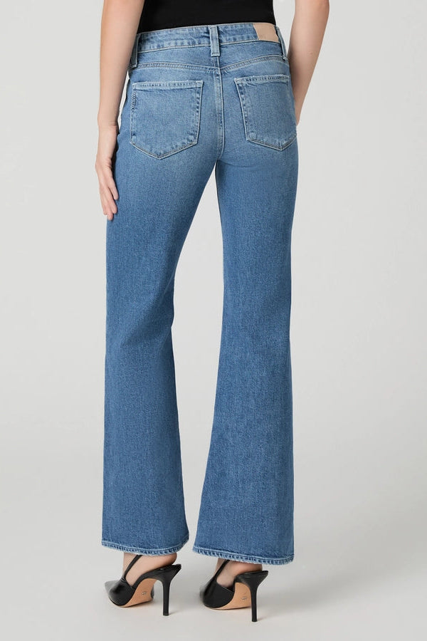 Rear view of a model wearing medium-wash blue flare jeans with black high-heeled sandals against a light gray studio background.
