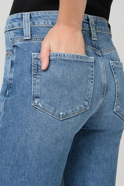 Close-up back view of a person wearing light blue denim jeans, with the hand in the back pocket, against a plain light gray background.