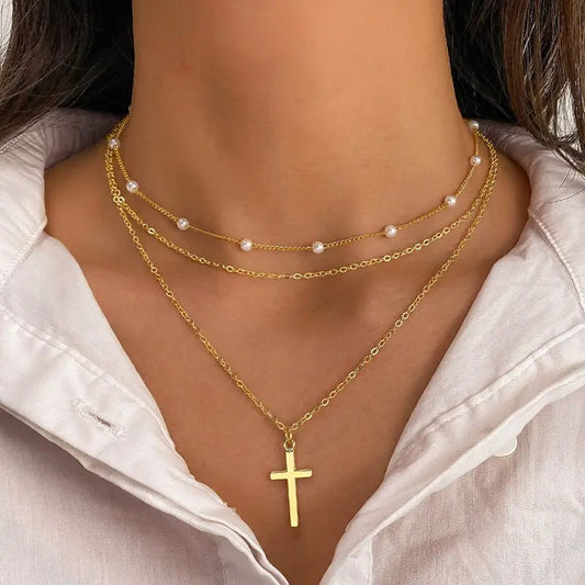 Gold necklaces with a cross pendant and pearl accents on a person wearing a white shirt.