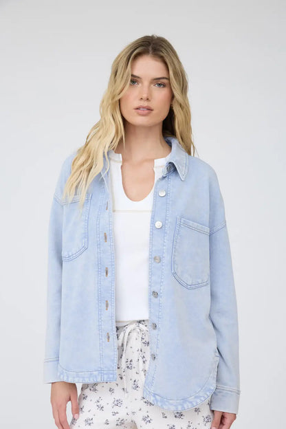 Woman wearing a light blue denim jacket over a white shirt with floral pants on a plain background