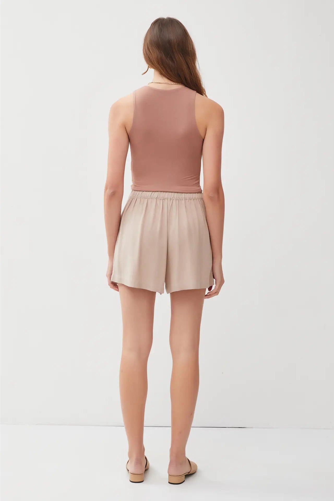 Woman wearing a brown sleeveless top and beige shorts on a white background