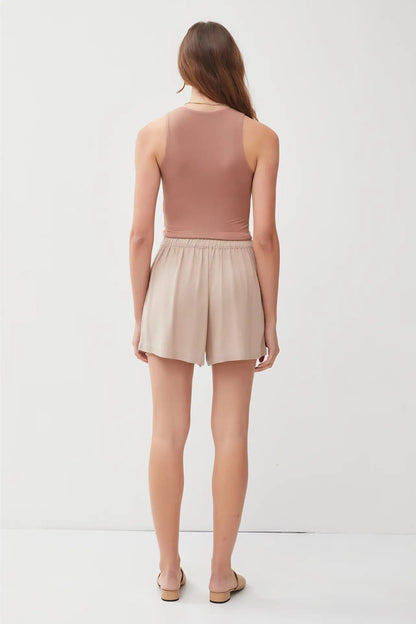 Woman wearing a brown sleeveless top and beige shorts on a white background