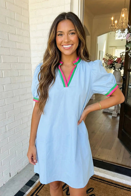 Woman wearing a light blue dress with pink and green accents in an indoor setting.