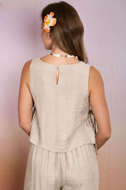 Woman wearing a beige sleeveless top and pants with a floral hair accessory against a gradient background