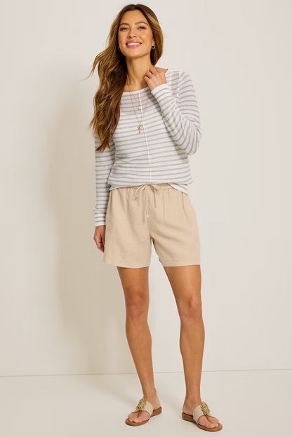 Woman wearing a striped long-sleeve top and beige shorts against a white background