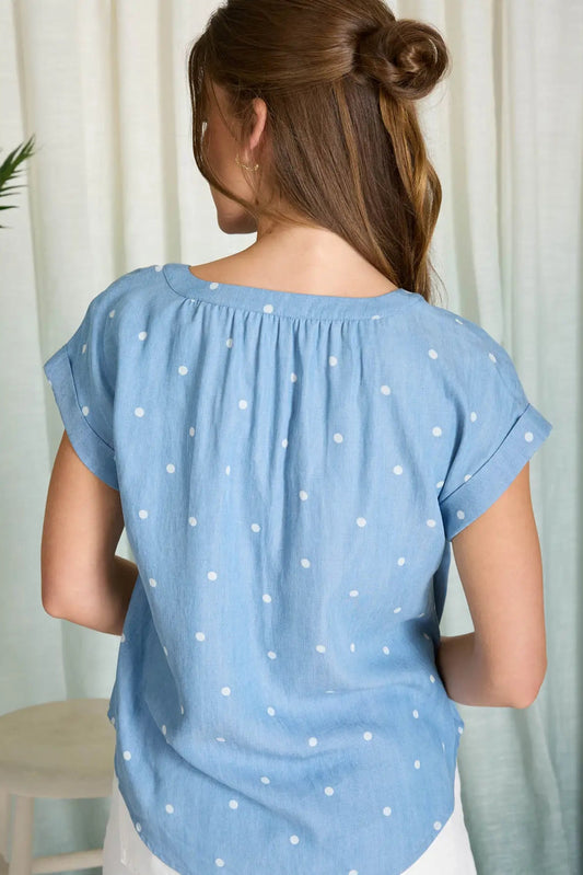 Woman wearing a blue polka dot blouse against a white curtain background