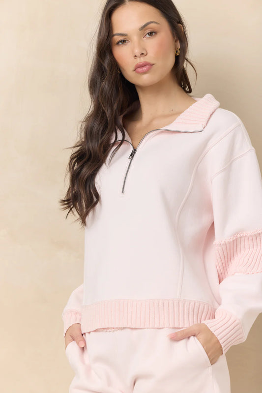 Woman wearing a light pink hoodie and pants against a beige background