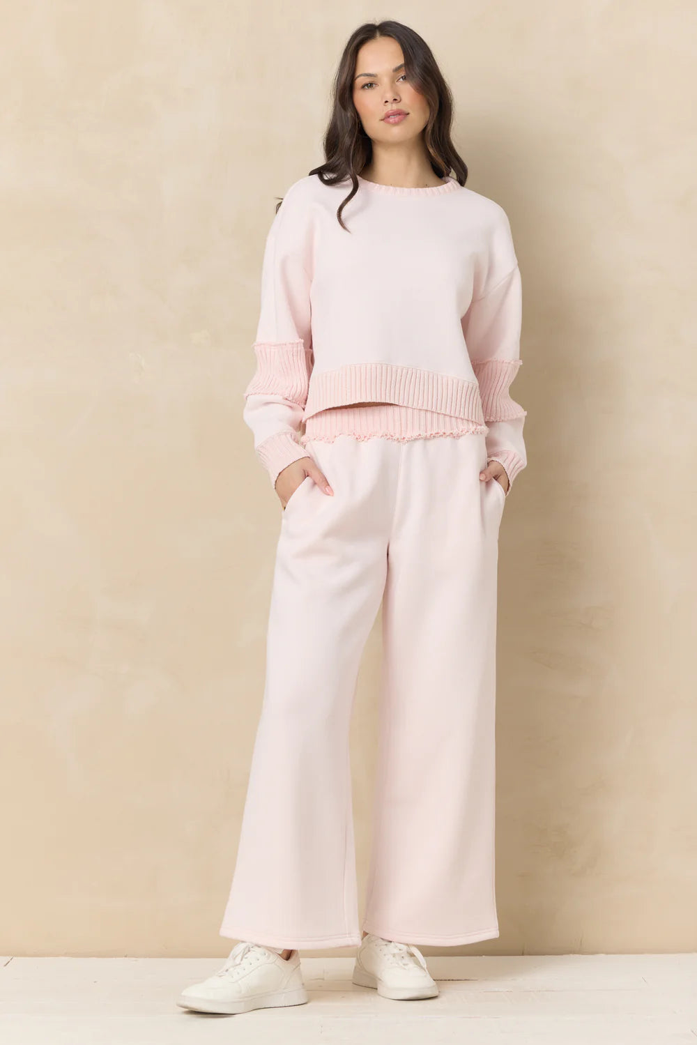 Woman wearing a pink sweater and white pants against a beige background