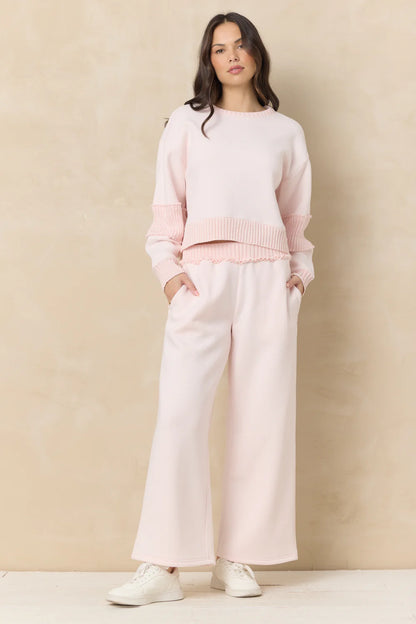 Woman wearing a pink sweater and white pants against a beige background