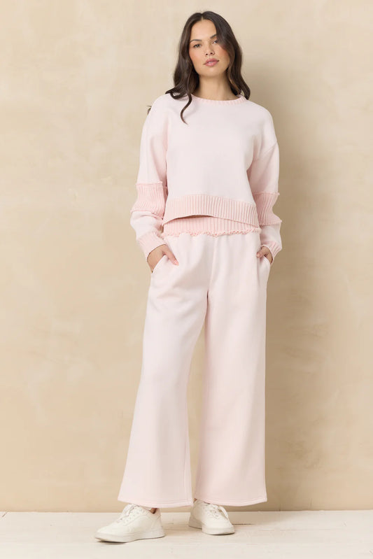 Woman wearing a pink sweater and white pants against a beige background