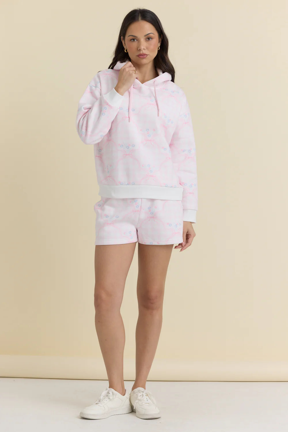 Woman wearing a pink hoodie and shorts set on a beige background