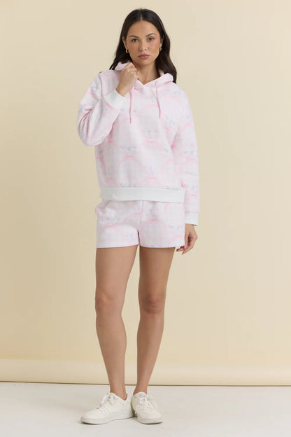 Woman wearing a pink hoodie and shorts set on a beige background