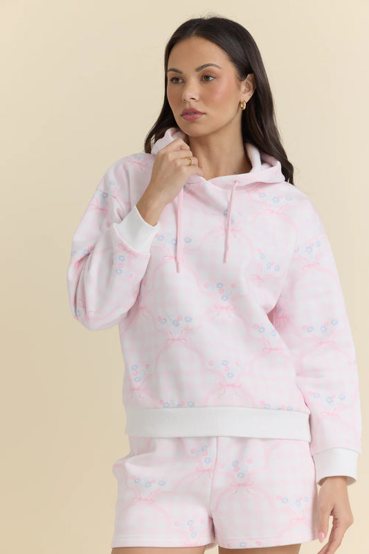 Woman wearing a pink hoodie and shorts set with a subtle pattern on a beige background