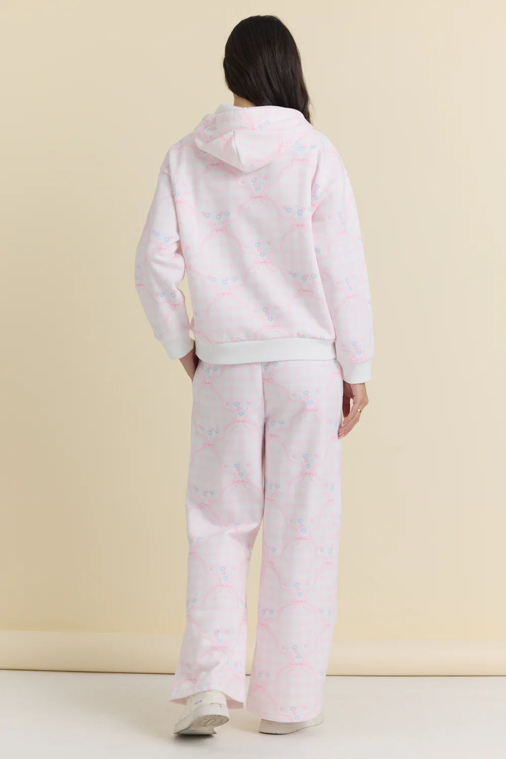 Person wearing a light pink hoodie and pants set on a beige background