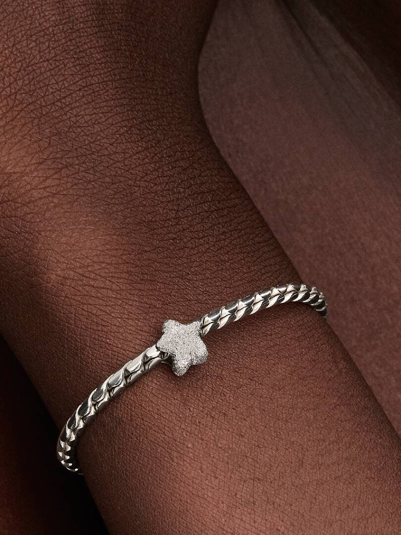 Silver bracelet with a star charm on a person's wrist against a brown background