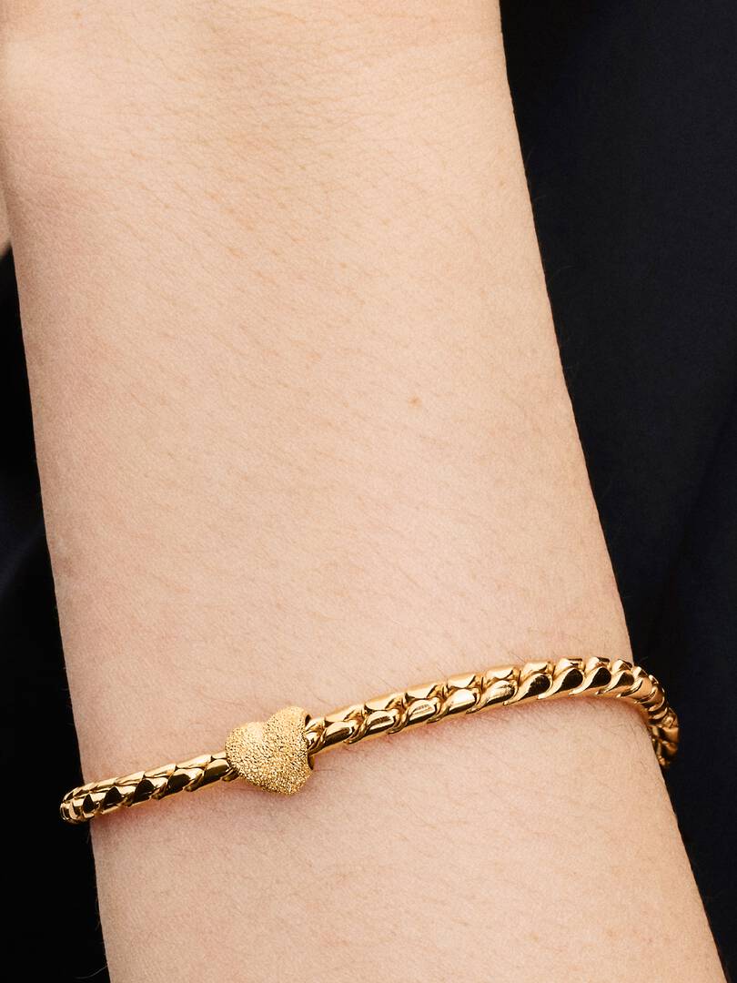 Gold bracelet on a wrist with a black background