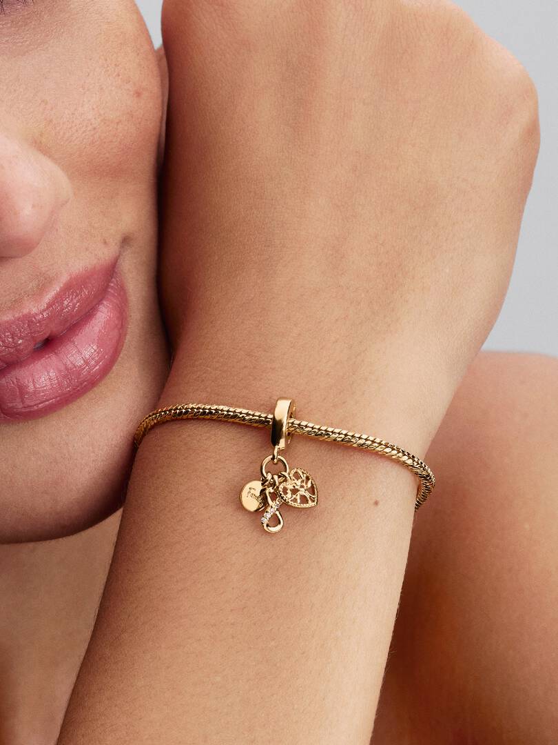 Gold bracelet with charms on a wrist against a neutral background