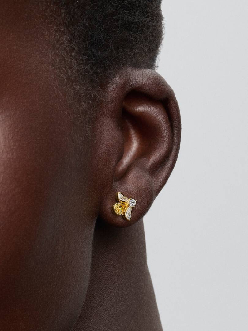 Gold bee-shaped earring on a person's ear against a neutral background