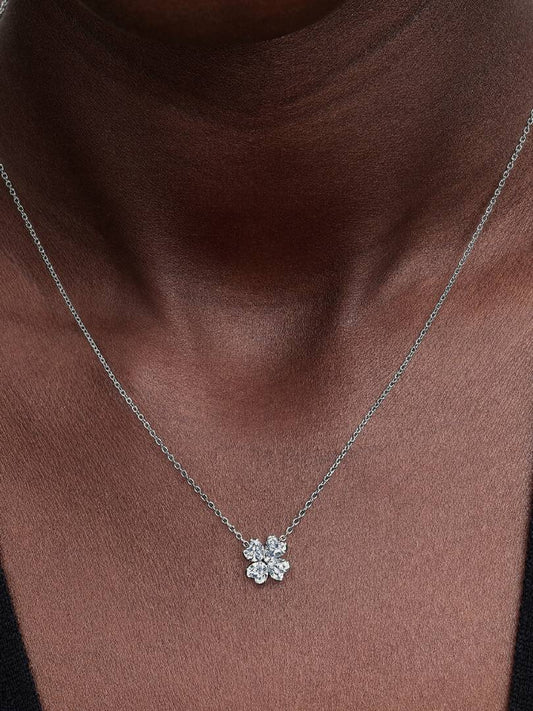 Silver necklace with a flower-shaped pendant on a person wearing a brown top.
