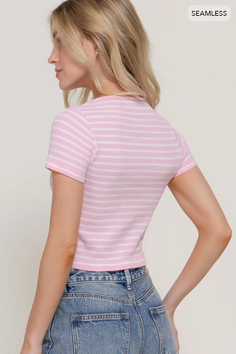 Woman wearing a pink and white striped shirt and blue jeans against a plain background