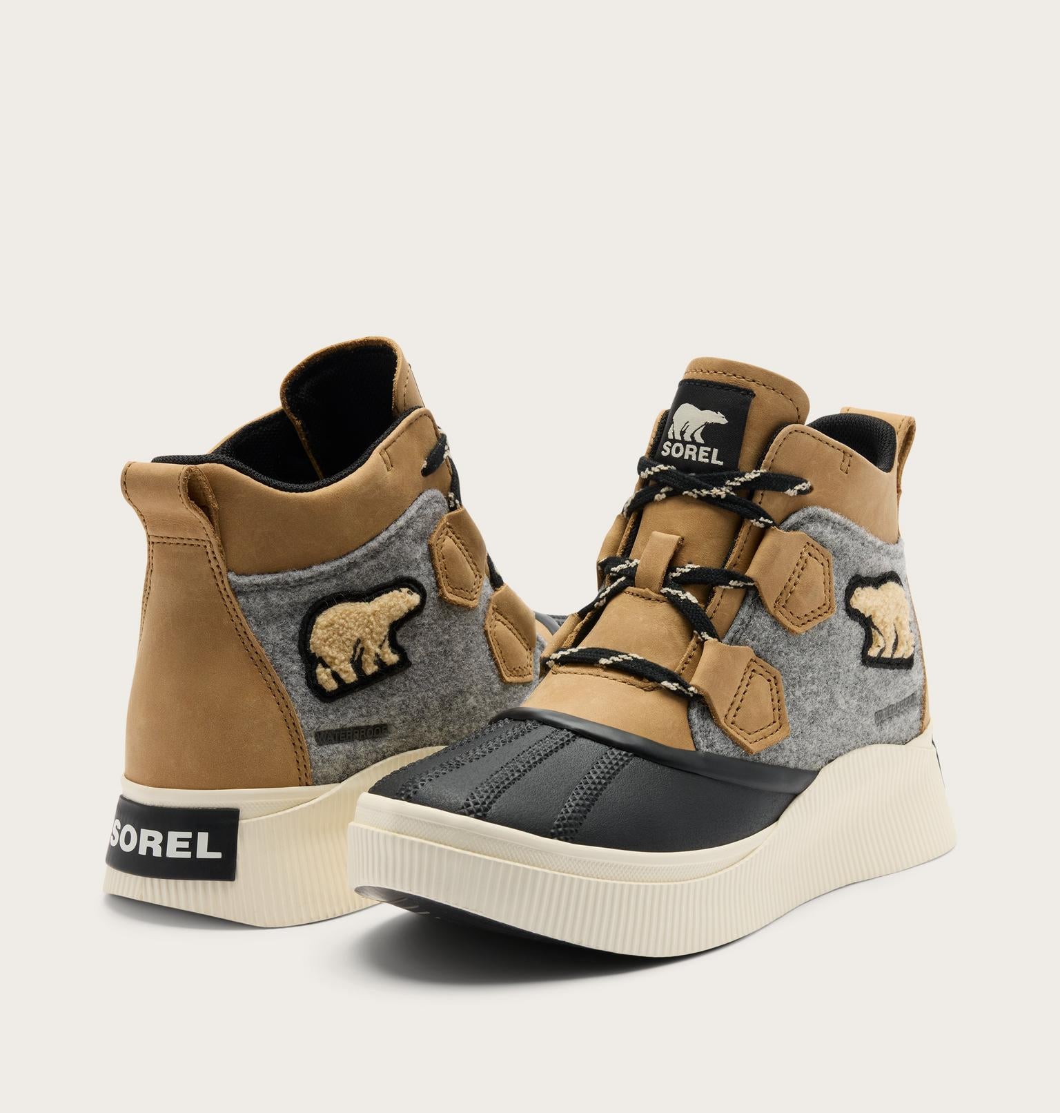 A pair of high-top sneakers by Sorel, featuring tan suede panels, a gray felt side panel with a bear patch, black rubber toe caps, and off-white soles. The brand name 'SOREL' is visible on the heel and tongue.
