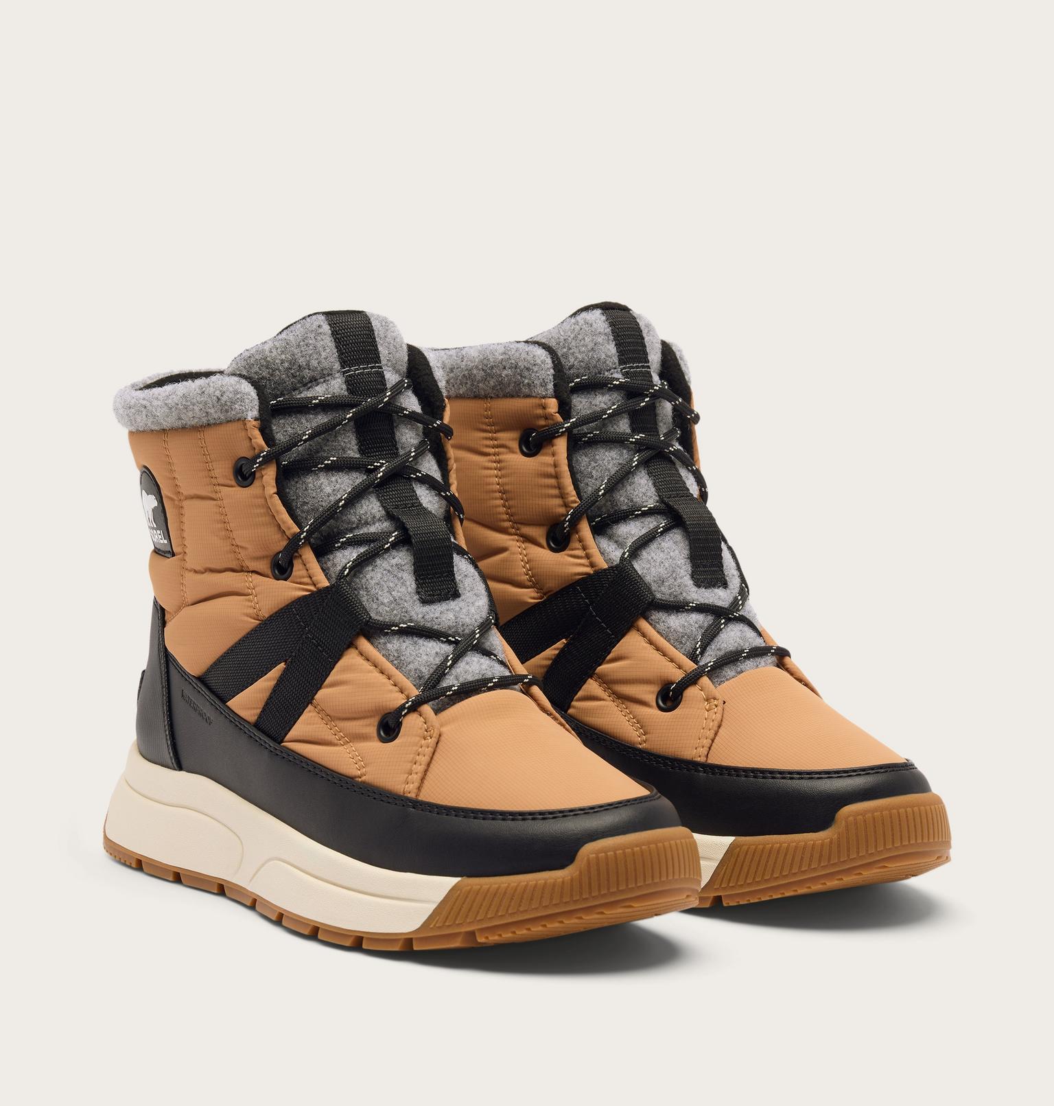 A pair of mid-height winter lace-up boots in tan and gray, featuring black straps and laces, a thick cream midsole, and a brown gum outsole, shown against a light beige background.