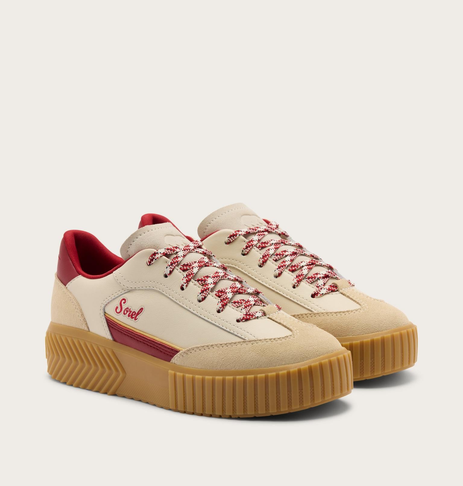 A pair of cream suede and canvas low-top sneakers with red accents, featuring red-and-white patterned laces, a red heel tab, and a thick brown gum sole. The brand name 'Soul' is embroidered on the side.