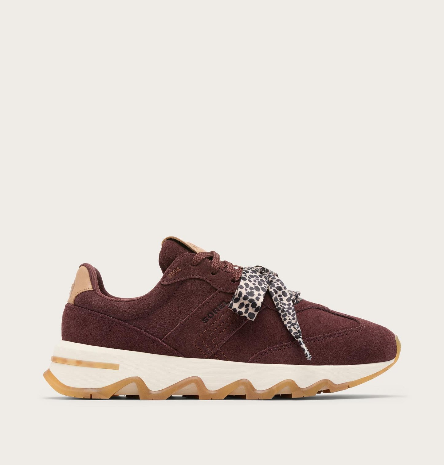 A low-top sneaker in burgundy suede and mesh, featuring a cream midsole with a gum outsole, a leopard-print ribbon tied around the laces, and tan heel and tongue accents, shown against a light beige background.
