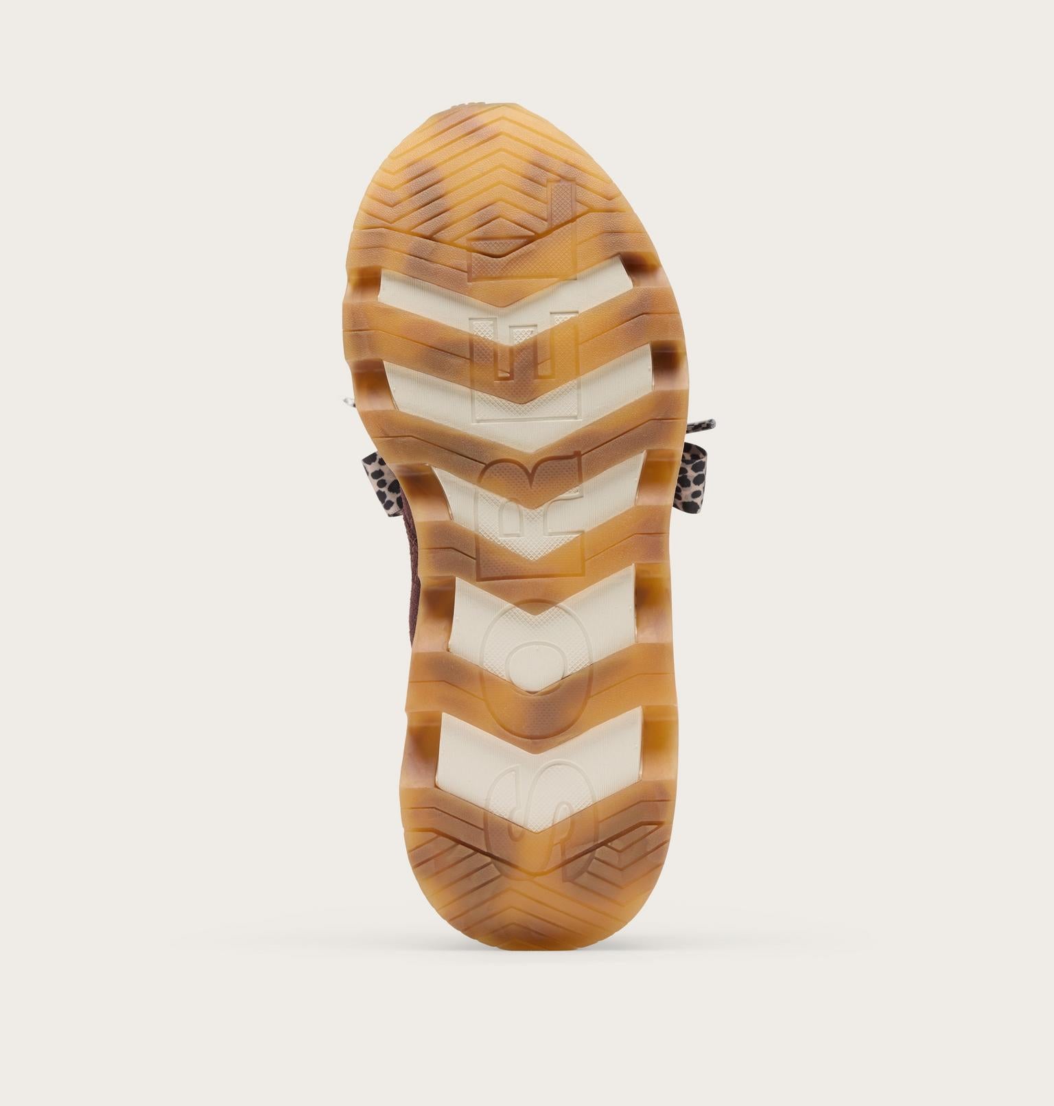 The outsole of a shoe shown from the bottom, featuring a translucent amber-brown and cream chevron pattern with a small leopard-print heel accent, photographed on a light beige background.