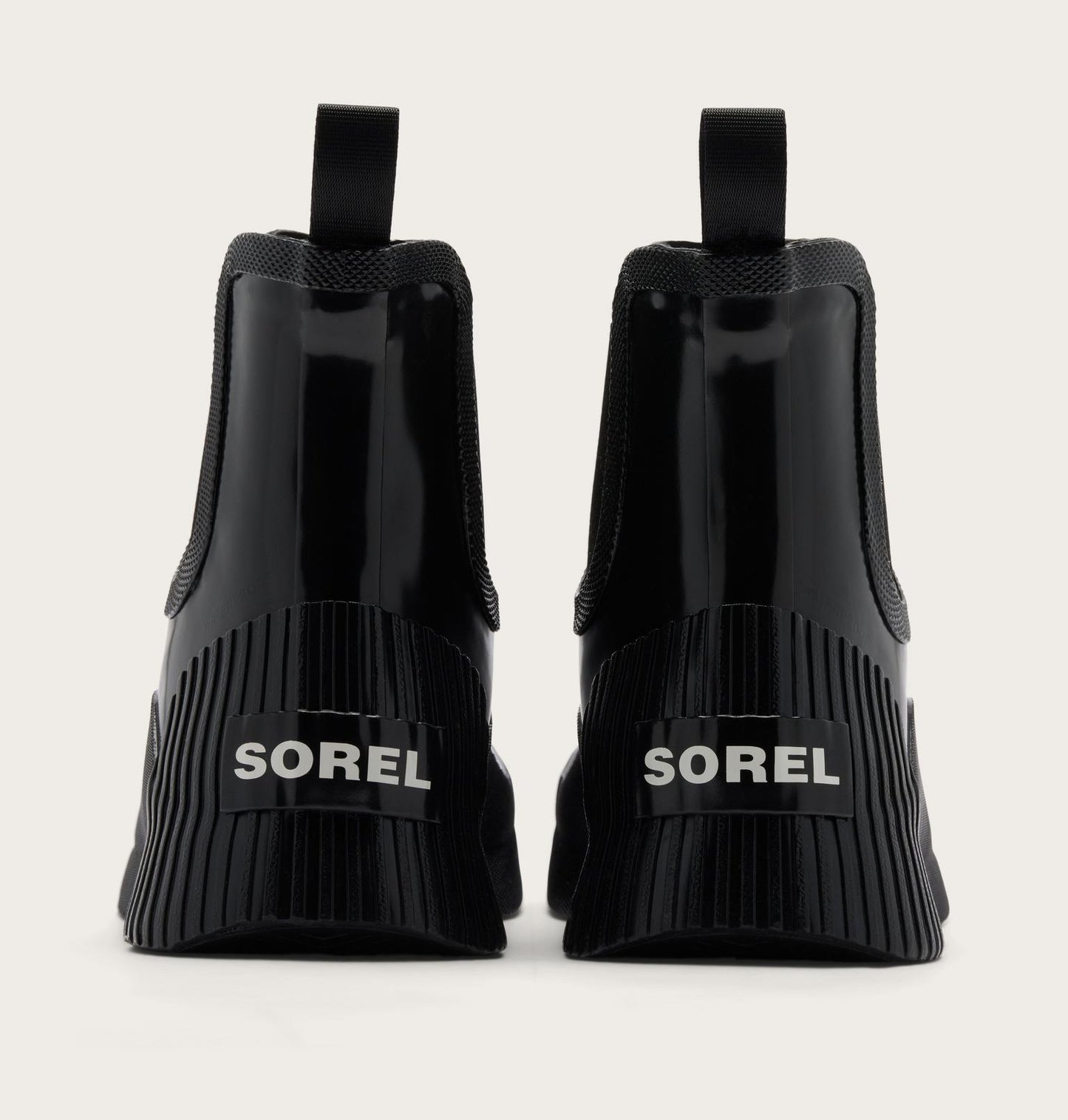 Black Sorel Chelsea-style ankle boots shown from the back, featuring a glossy patent leather front, elastic side panels, and a thick ribbed sole with the SOREL logo in white.