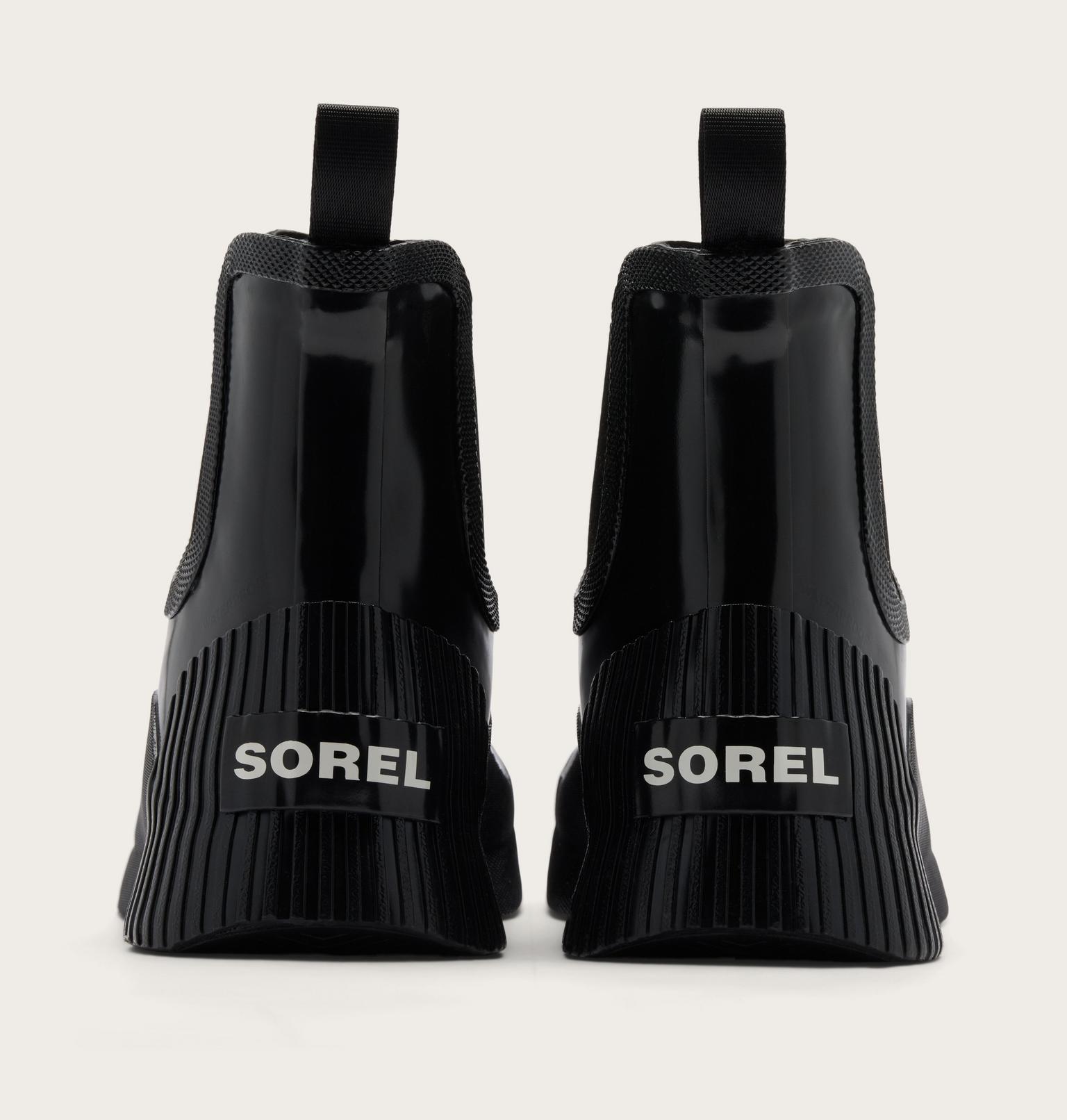 Black Sorel Chelsea-style ankle boots shown from the back, featuring a glossy patent leather front, elastic side panels, and a thick ribbed sole with the SOREL logo in white.