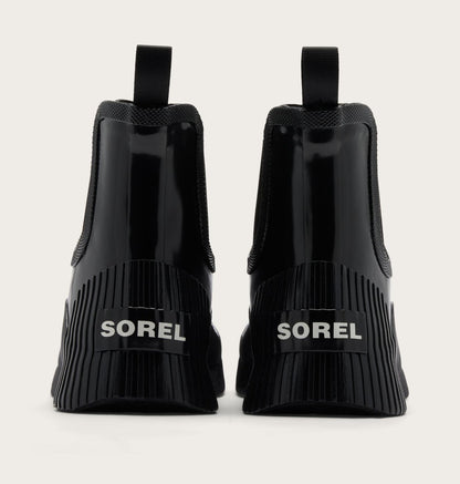Black Sorel Chelsea-style ankle boots shown from the back, featuring a glossy patent leather front, elastic side panels, and a thick ribbed sole with the SOREL logo in white.