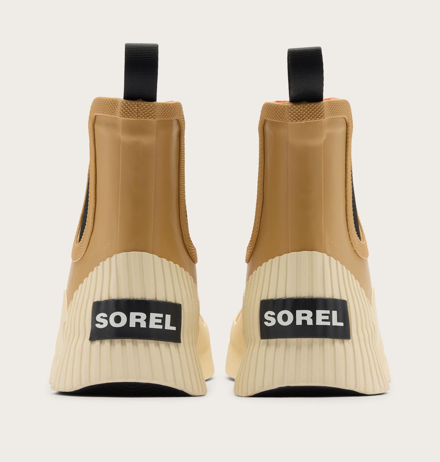 A pair of Sorel ankle boots shown from the back, featuring a tan upper, cream ribbed sole, and black pull tabs and logo patches.