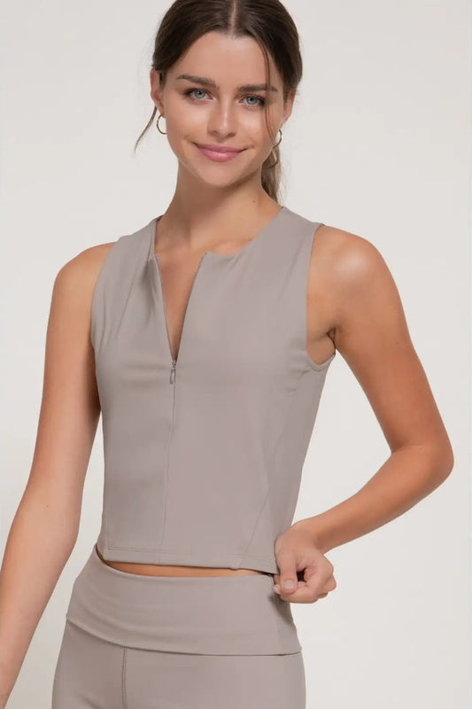 Woman wearing a sleeveless beige top on a plain background
