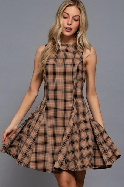 A woman modeling a sleeveless, high-neck, flared skater dress in a brown and beige plaid pattern against a solid gray studio background.