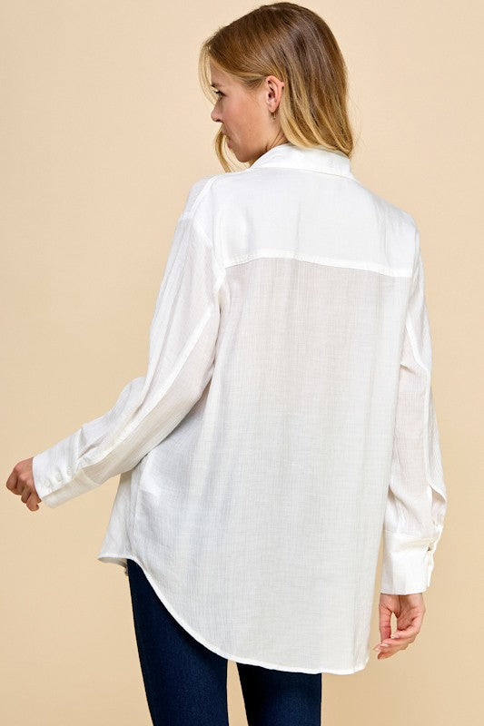 Woman wearing a white sheer blouse over a dark top against a beige background