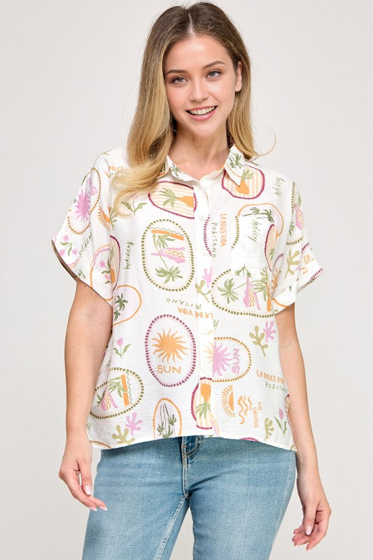 Woman wearing a white blouse with colorful patterns and blue jeans on a plain background