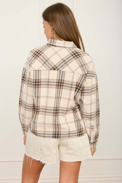 A woman shown from the back wearing a cream-colored plaid button-up shirt with brown and black lines, paired with off-white shorts, against a white paneled wall.