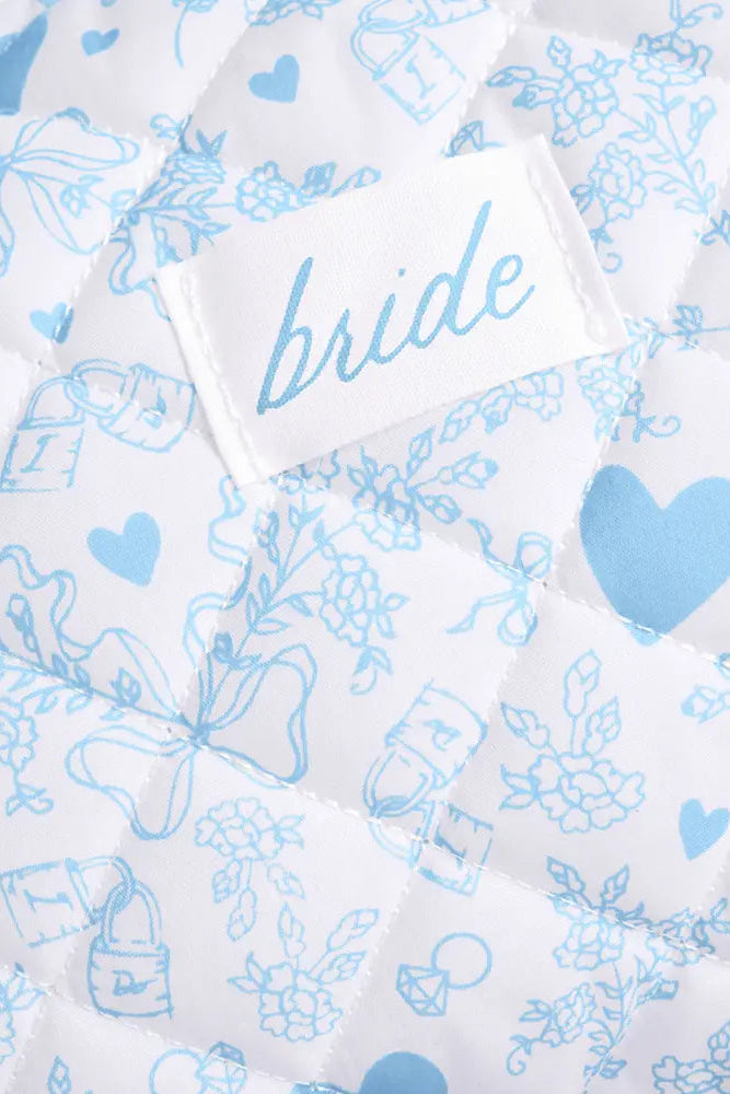 Close-up of a white quilted fabric with light blue floral and heart patterns, featuring a sewn-on label that reads 'bride'.